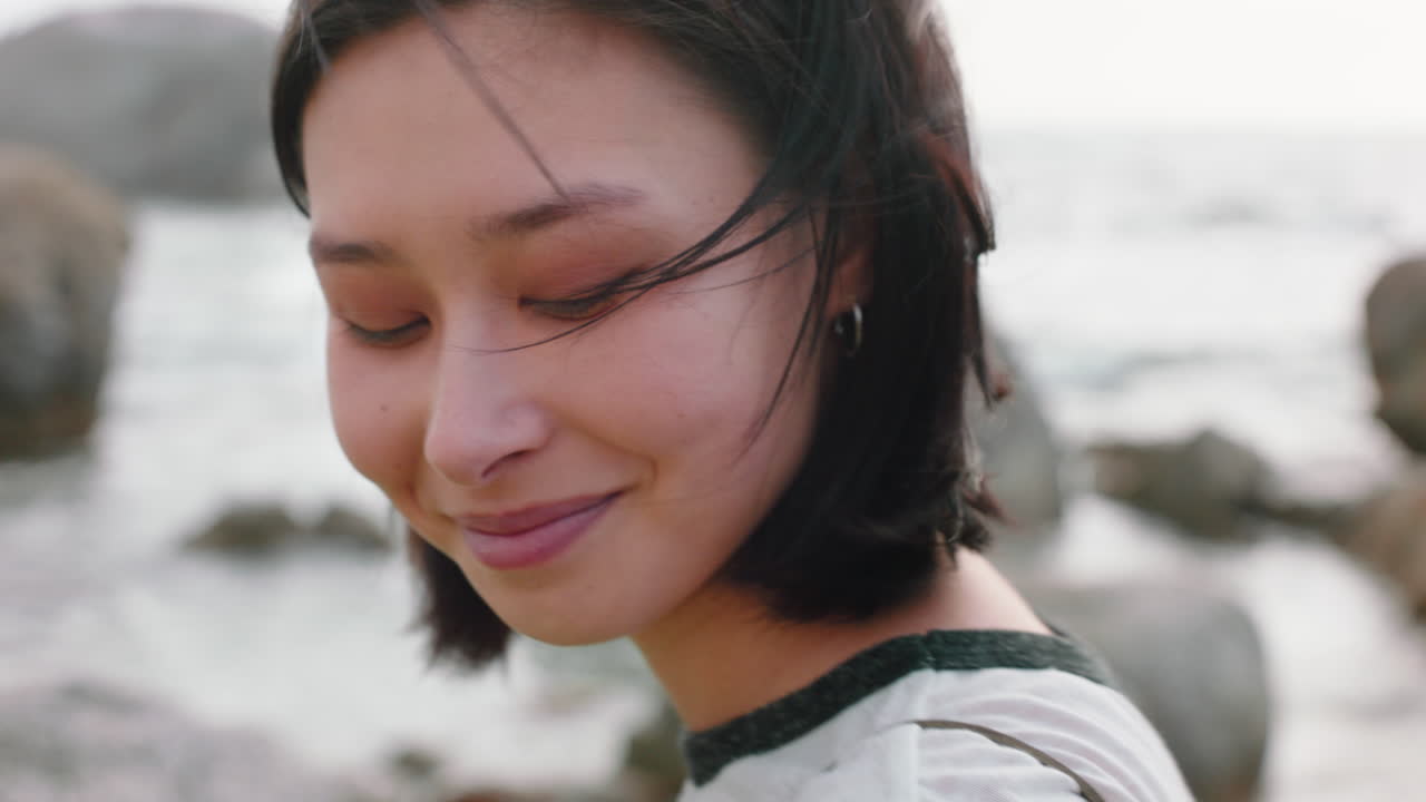 아름다운 아시아 여성의 초상화 미소 짓고 구름진 해변을 즐기며 바람이 불고 있는 해변에서 머리카락을  ⁇ 는 휴가 생활 방식을 탐구합니다.