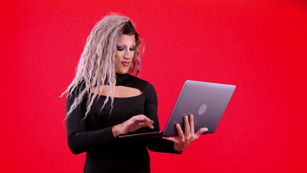 Drag queen using a laptop on a red background