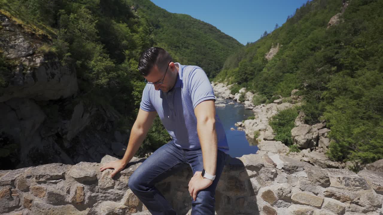 Tourist sitting on the side railings of the Devil's Bridge, located right above the beautiful Arda River, located next to the Rhodope Mountains in Ardino, Bulgaria
