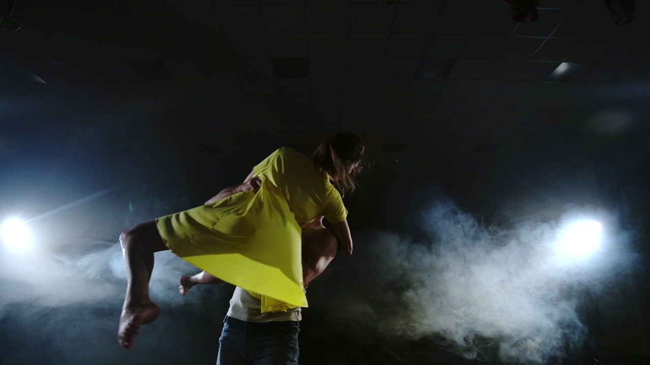 la telecamera sta zooming e sparando da pieno scatto a medio uno in lento mong una giovane ragazza in un vestito giallo e un uomo in una camicia bianca ballando sul palco sotto i riflettori e il fumo