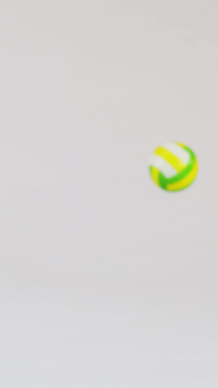 Small colorful volleyballs bounce across a clean white studio floor with soft even lighting