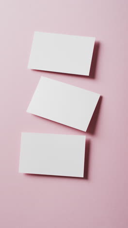 vertical video of three white business cards arranged on pink background, copy space, slow motion