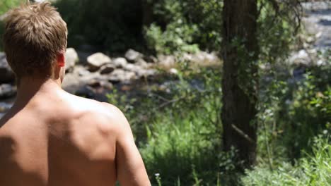 slow motion shot of a shirtless man practicing his axe throwing skill by trying to throw his hatchet at a pine tree