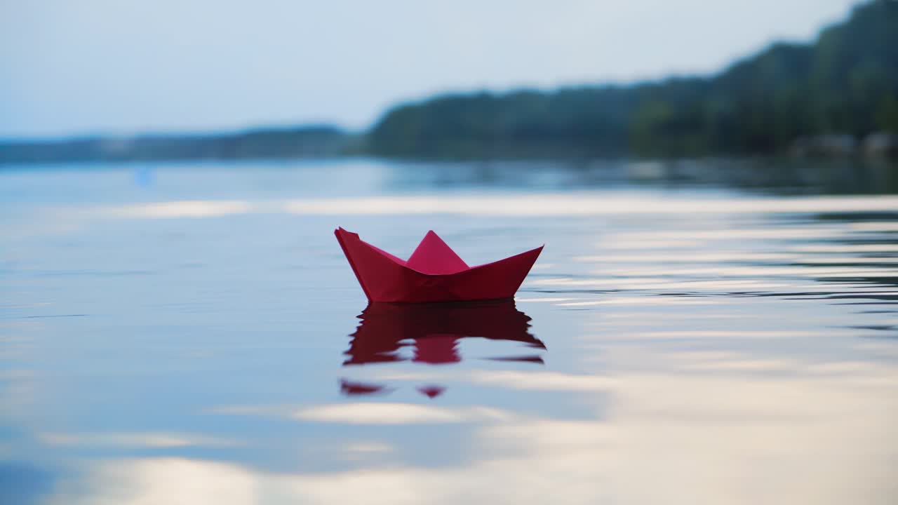 Alone homemade ship spinning on the evening river on the beautiful natural background. One red paper boat floating on the water surface