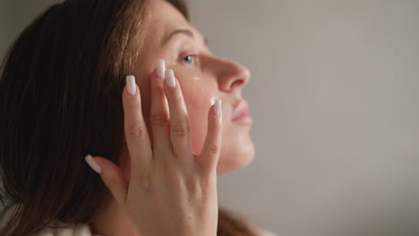 mujer aplicando crema de gel a la cara en el baño. joven dama morena con manicura aplica crema hidratante para la cara después de tomar la ducha en cámara lenta