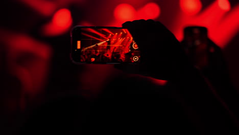 Enthusiastic crowd at a concert captures electrifying moments on smartphones, showcasing vibrant red and white stage lighting and live music atmosphere