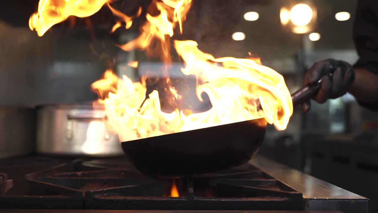 el chef arroja verduras en una sartén que produce llamas sobre el horno