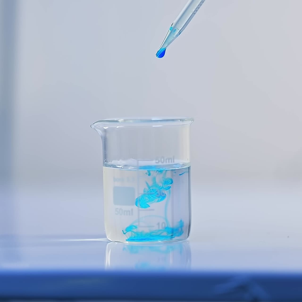 Beaker with water is placed on the laboratory table. A few drops of blue liquid are poured into the water. The examination of diapers process