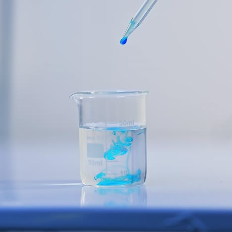 beaker with water is placed on the laboratory table. a few drops of blue liquid are poured into the water. the examination of diapers process