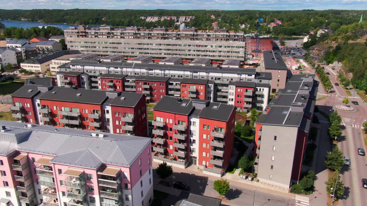Bright aerial orbit of striking red and pink apartment buildings with green areas and lake distant in Gustavsberg