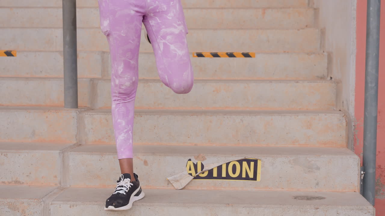 Woman balancing on one foot near caution sign, purple leggings and black sneakers, stair edge focus on stability and ankle control, practice drill on concrete steps, urban training vibe