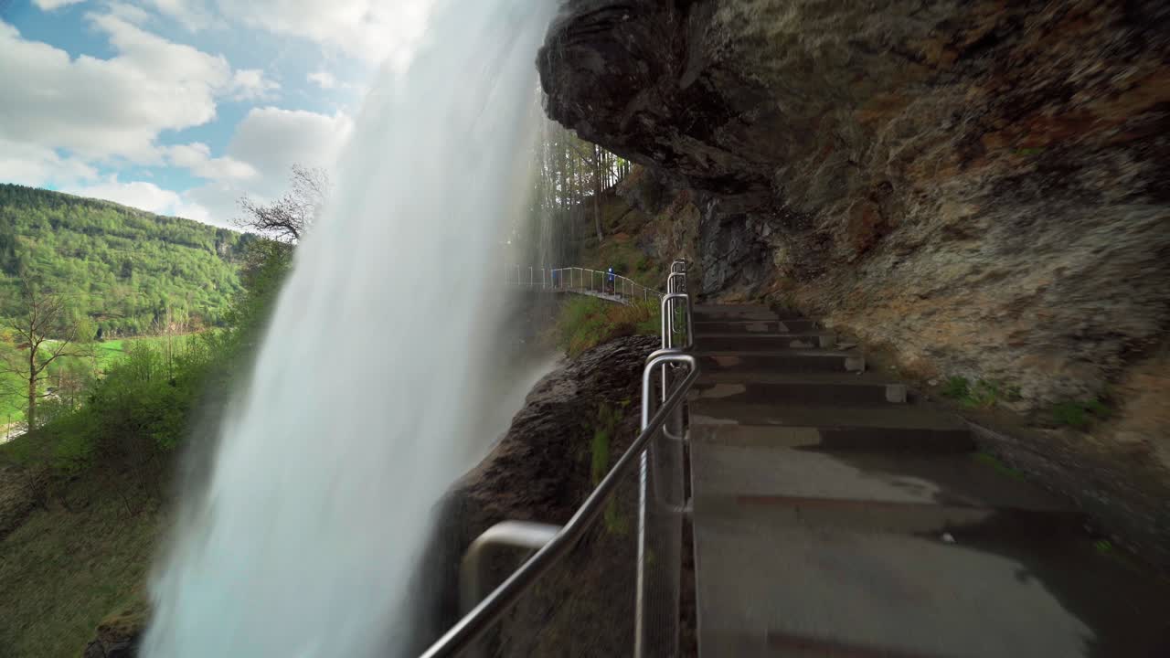 A famous Steinsdalsfossen waterfall in the village of Steine, Norway.  The wall of turbulent whitewater falling off the mountain. The pedestrian bridge is leading under the waterfall