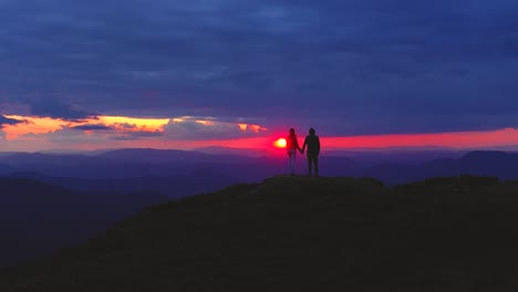 the couple standing on the mountain on a sunset background