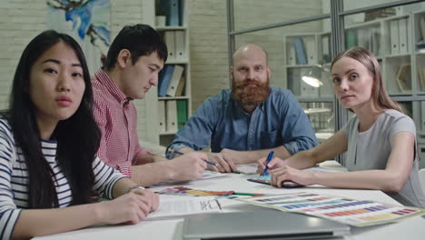 group of coworkers sitting on the table in a business meeting while they looking at camera