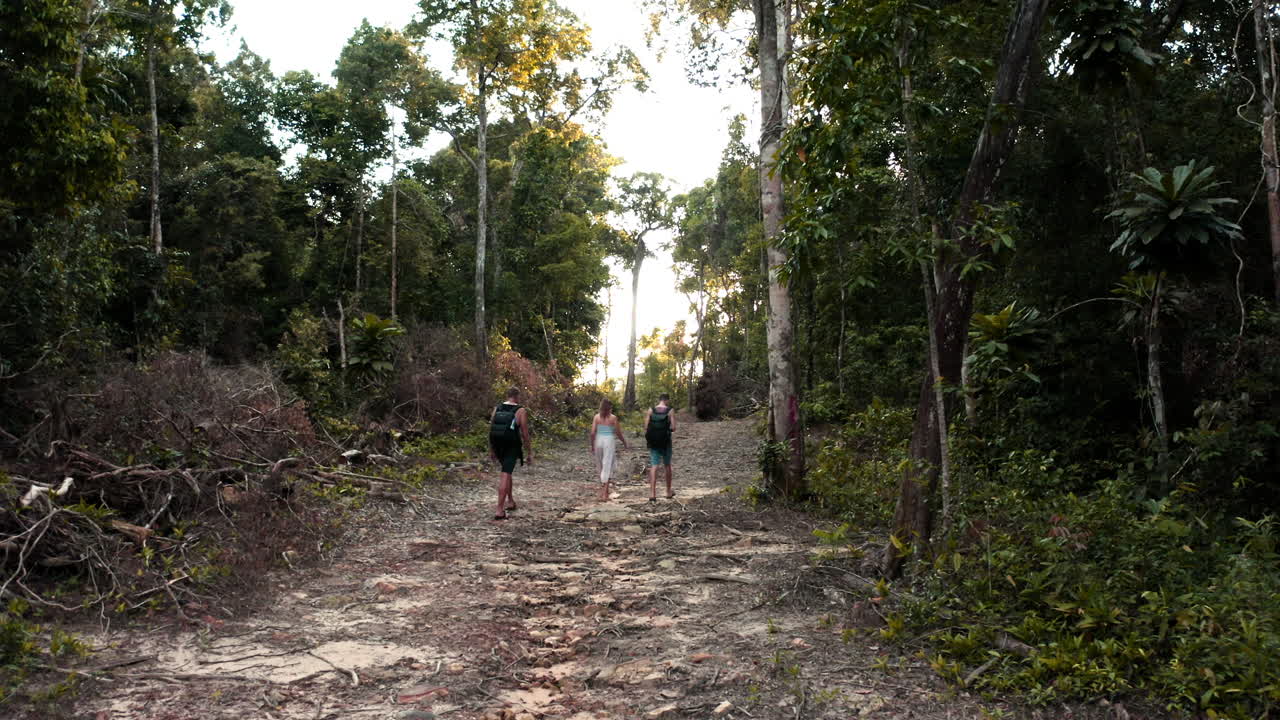 Three young people walking through a hidden jungle path to tropical Lazy Beach Cambodia, aerial