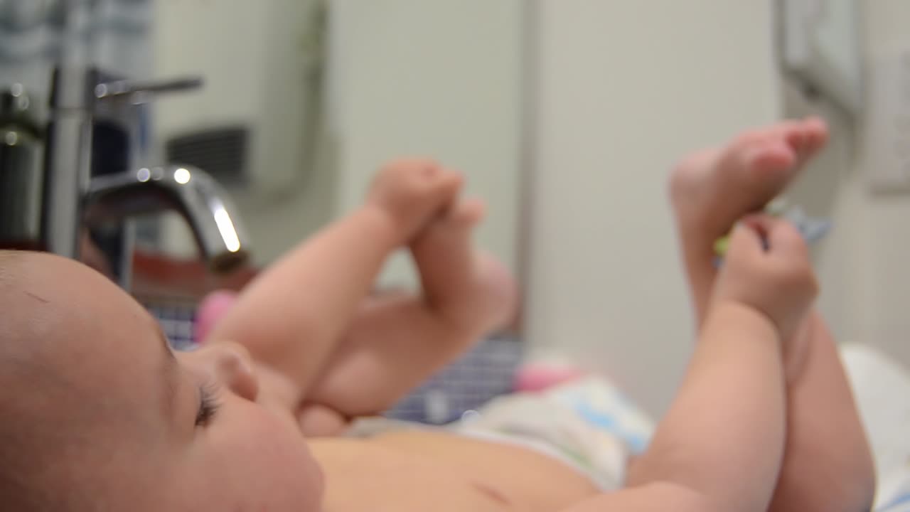 Bambino di sei mesi carino che gioca con il ciuccio e i suoi piedini nel bagno