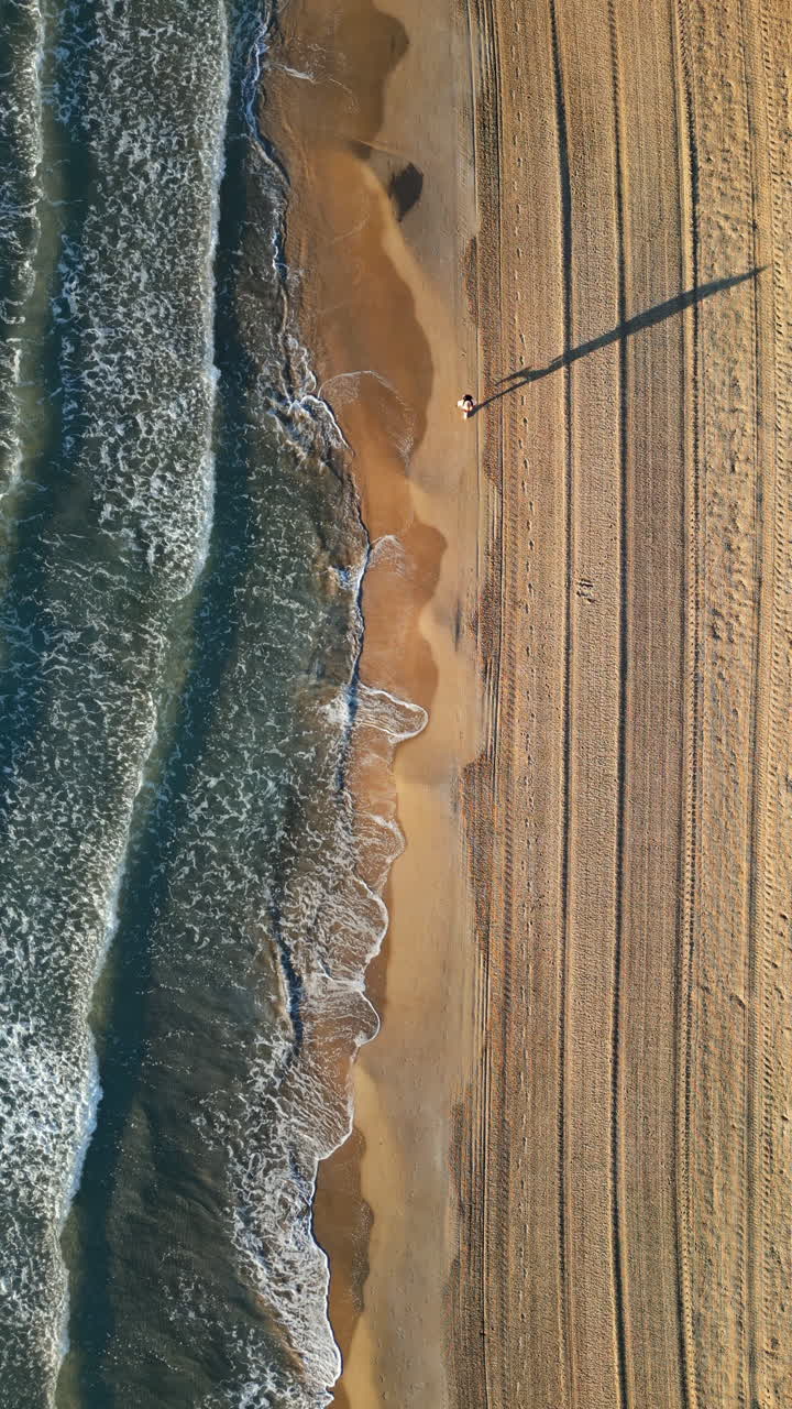 Uomo che cammina sulla spiaggia con le onde che si infrangono sulla riva ad Alicante, Spagna. Verticale