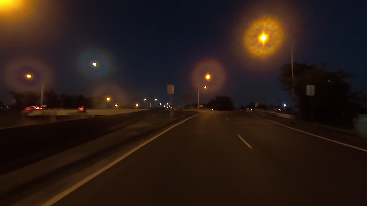 Punto di vista (POV) di guida notturna posteriore per la sostituzione su green screen di una scena interna all'auto - svolta a sinistra in una grande rotonda con traffico minimo.