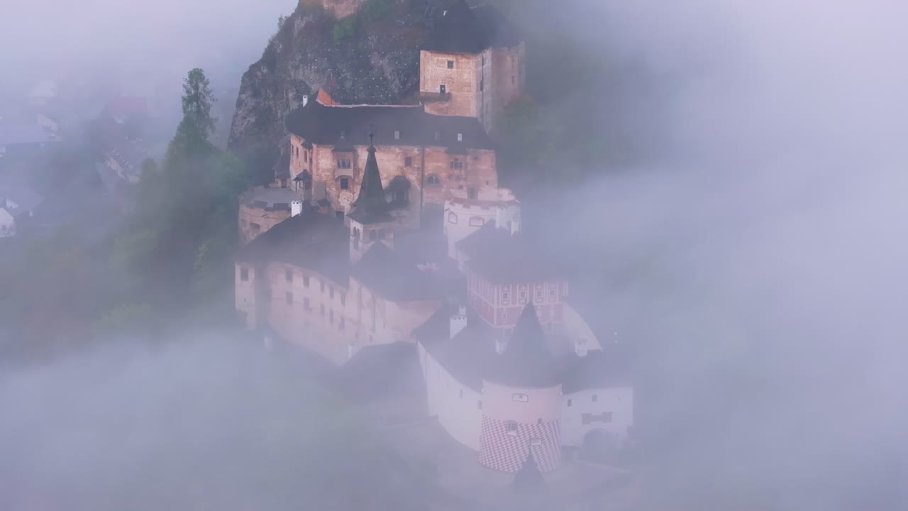 Imágenes de dron del Castillo de Orava rodeado de colinas ondulantes y brumosas