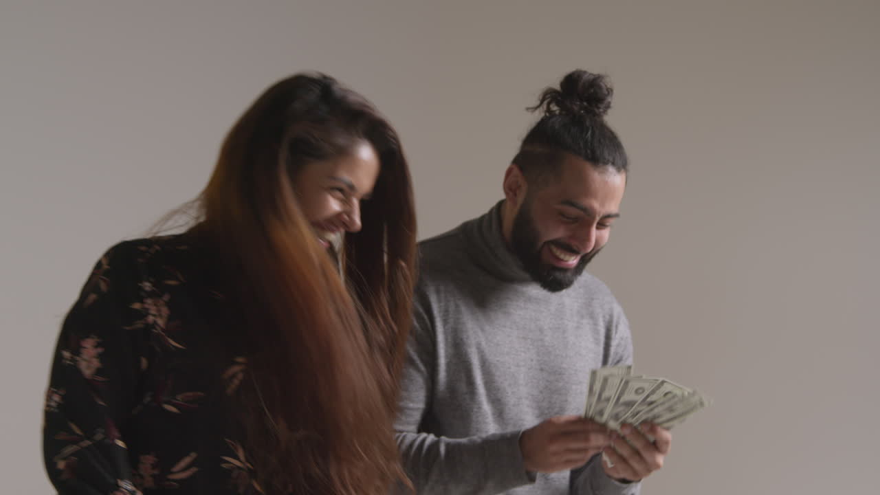 흥분한 커플이 현금 상을 수상한 것을 축하하면서 공중으로 100달러 지폐를 던지는 스튜디오