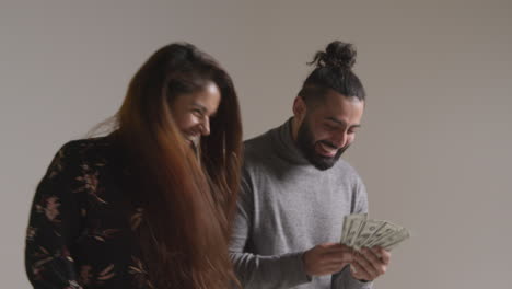 studio shot of excited couple celebrating winning cash prize throwing handful of 100 dollar bills in the air