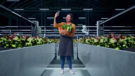 full body of asian female farmer with vegetable basket taking selfie by smart phone in smart farm