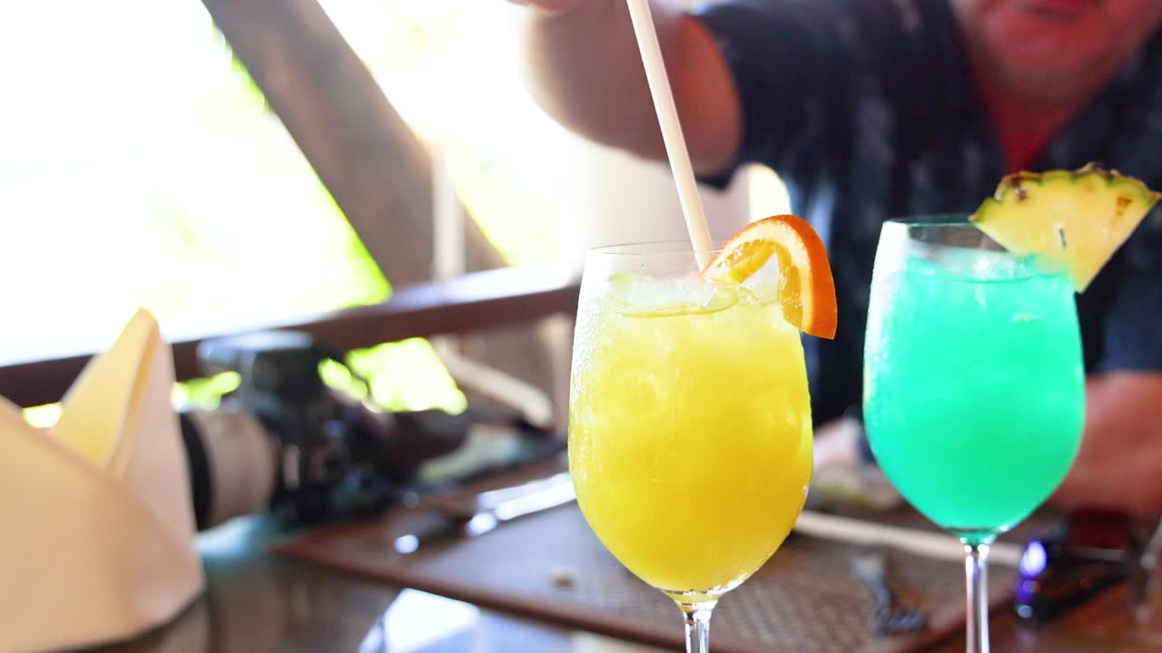 Two vibrant cocktails with fruit garnishes on a sunlit table, capturing a relaxed, tropical atmosphere