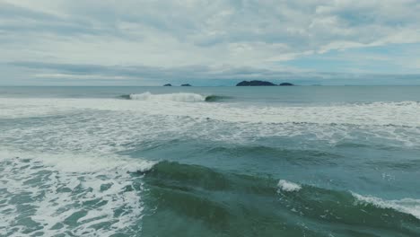 Dolly-Towards-Open-Sea-with-Waves-Crashing-onto-Sandy-Beach,-Summertime-Day