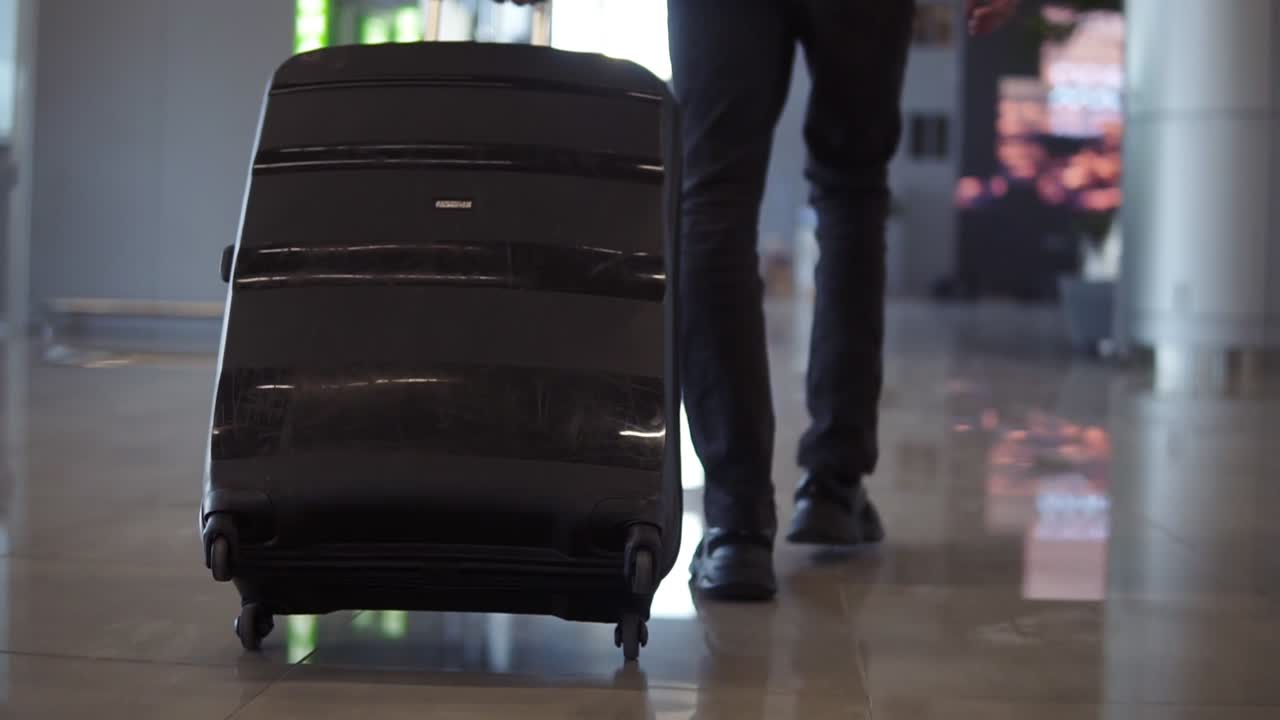 Close up, cropped shot of man legs with the black baggage walking to the airport terminal. Slow motion. Rare view