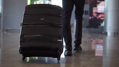 Close-up,-cropped-shot-of-man-legs-with-the-black-baggage-walking-to-the-airport-terminal.-Slow-motion.-Rare-view