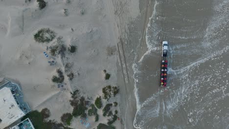 aerial top down drone shot of truck with trailer and atv's driving on pismo beach california sand beach at sunrise