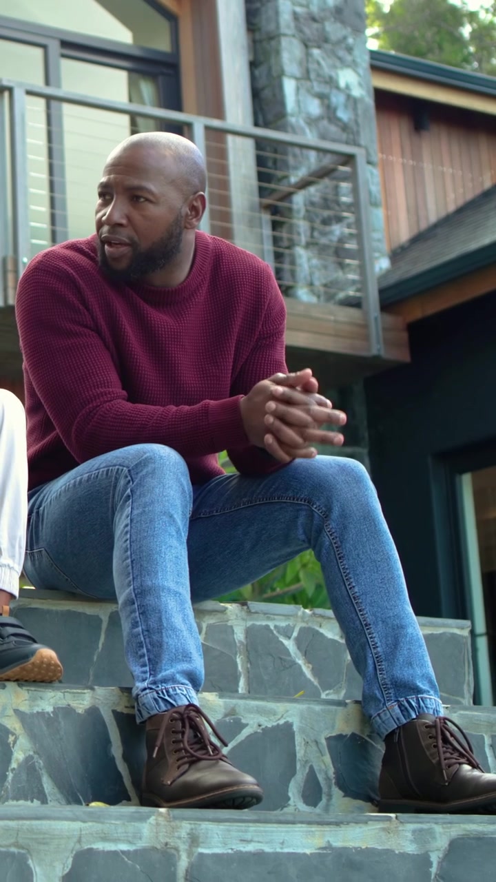Vertical video: Turning man in red top talking and leaning on stone steps at home as child talking