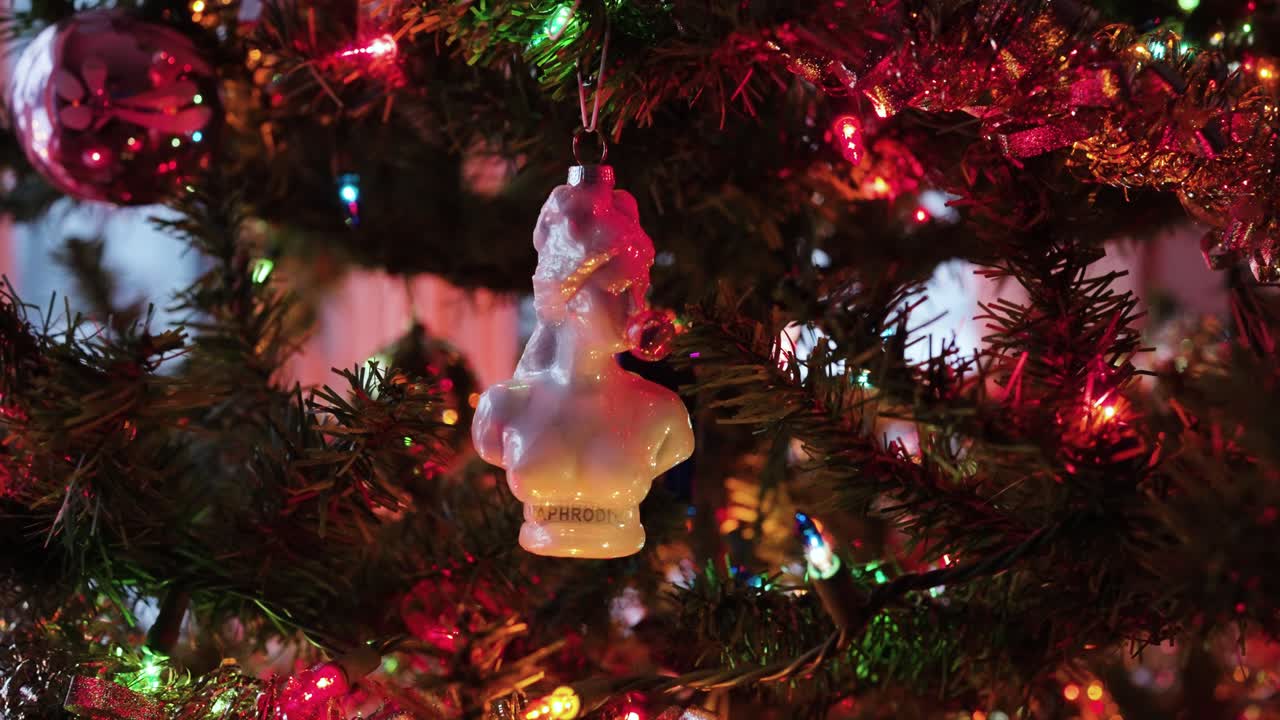 Aphrodite blowing bubble gum: Christmas Tree Statue Ornament hanging with lights around it.
