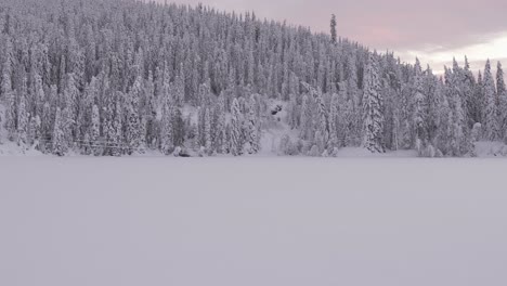 Panoramic-shot-of-frozen-Lake-Mylla-with-white-pine-trees-covered-with-snow-and-mountains-in-Norway
