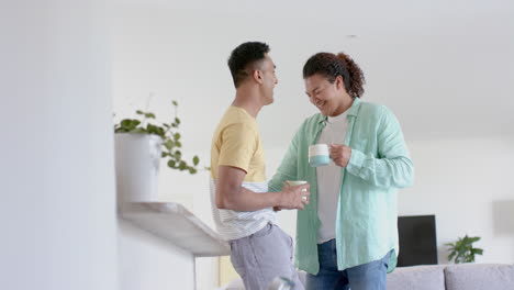 happy diverse gay male couple having coffee, standing and talking at home, copy space, slow motion