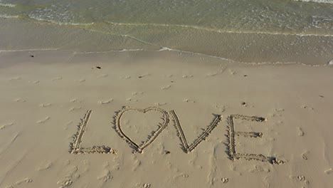 a turning shot of love inscribed in the sand on a beach