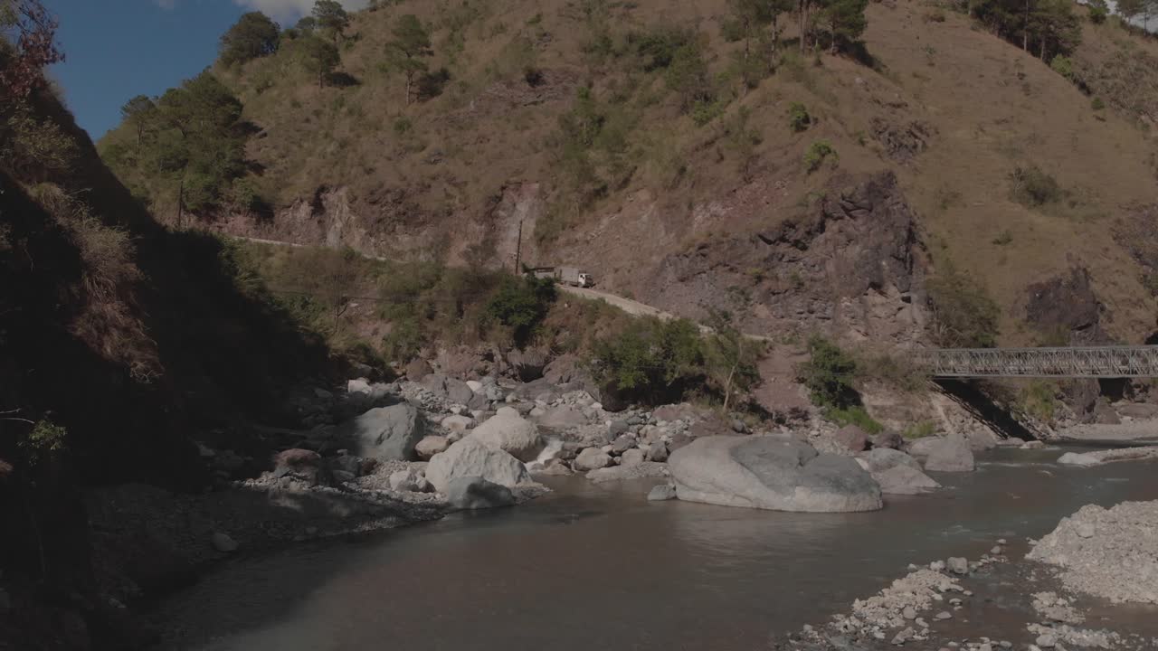 rocky river winding through mountains in canyon valley water flowing approaching grey boulders green trees blue sky slow aerial smooth moving forward proximity to electrical wires