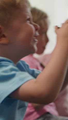 blond toddler talks while playing video game with elder sister at home on blurred background. happy children jump feeling happy to win closeup