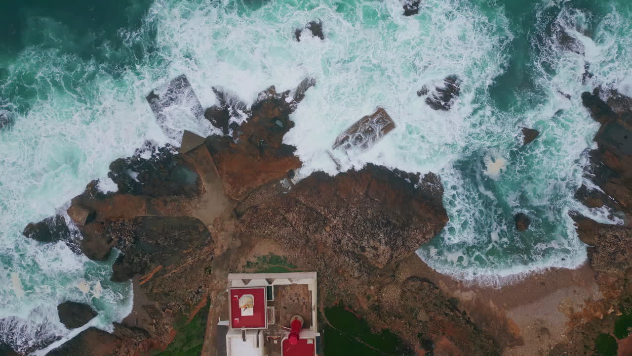 Waves washing lighthouse cliff top view. Aerial shot high beacon at shore rocks