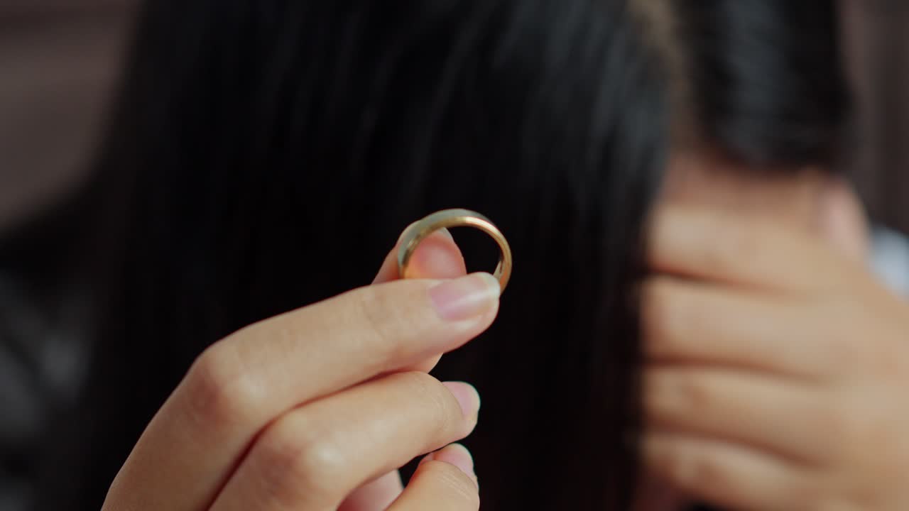 Primo piano di una moglie sconvolta che tiene un anello nuziale d'oro mentre piange con sfondo sfocato