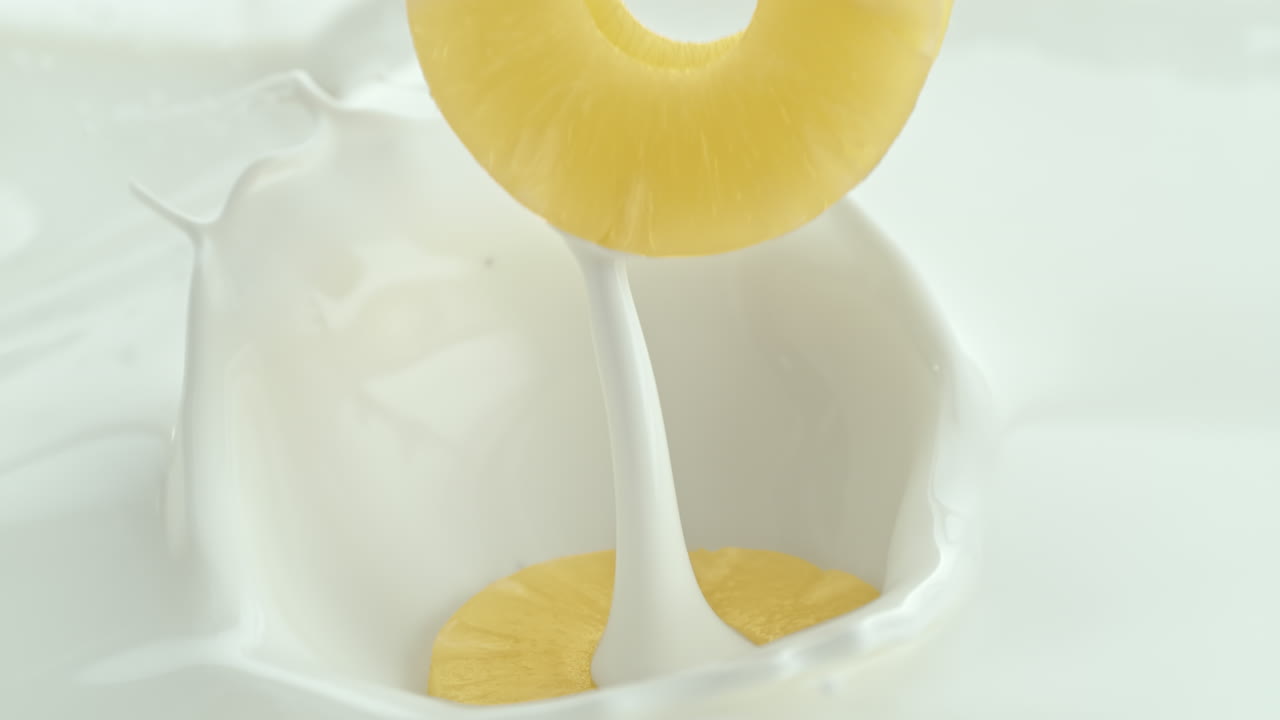 크림 우유에 떨어지는 파인애플 조각은 매크로와 느린 동작으로 스프레이를 만니다.