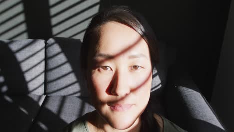 Thoughtful-asian-woman-sitting-on-sofa-close-to-window-at-home