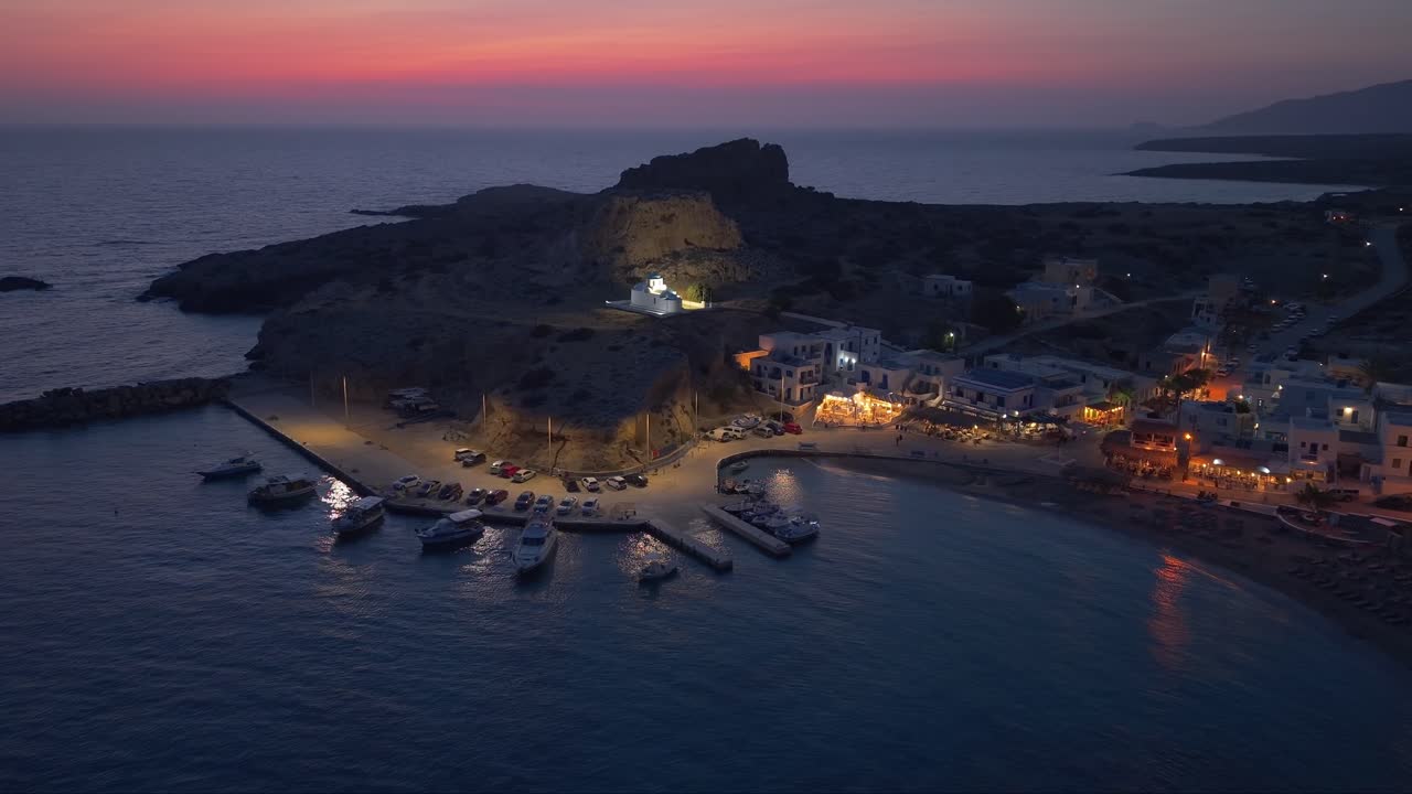 Aerial drone captures the calm atmosphere of twilight above Finiki village in Karpathos, with a colorful evening sky reflecting over the serene Aegean coast