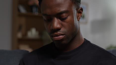 close up of unhappy and depressed young man sitting on sofa at home messaging or browsing on mobile phone 1