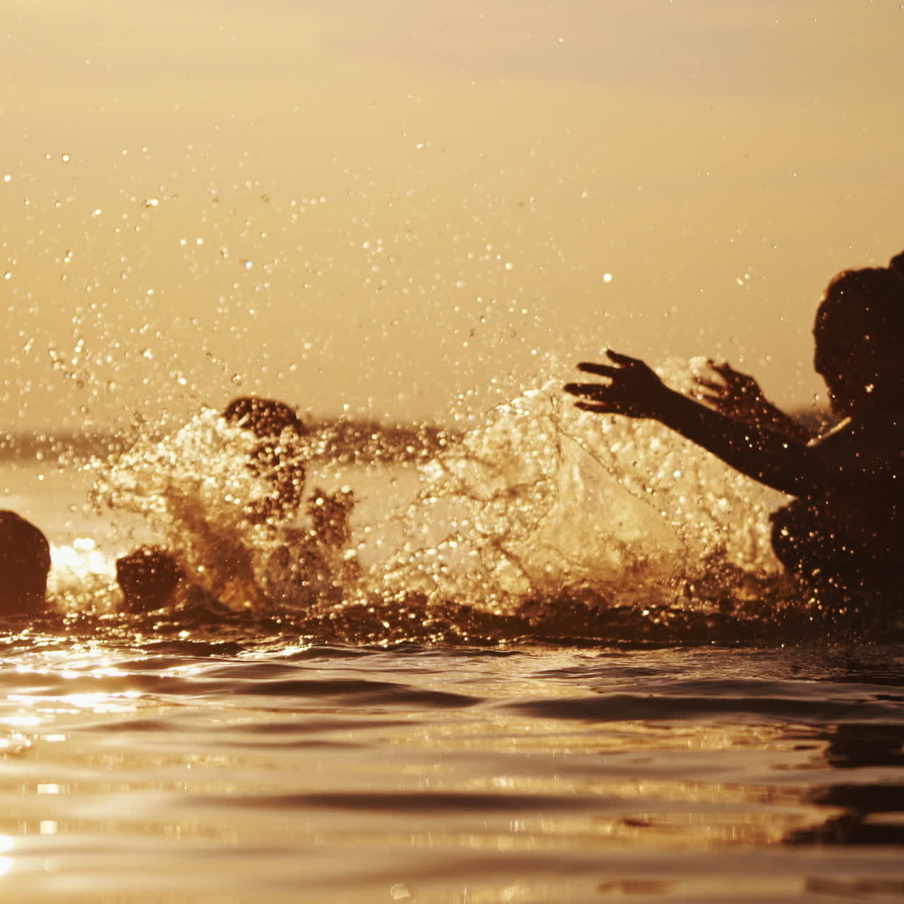 Happy children playing in the river with mother. Silhouette of a woman splashing water on boys in the evening at sunset. Happy summertime.