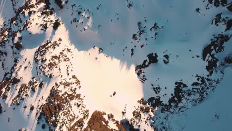 Una-Amplia-Toma-De-Drones-De-Arriba-Hacia-Abajo-De-Un-Pico-Nevado-En-Las-Montañas-Olímpicas-Tomada-Desde-Las-Afueras-Del-Parque-Nacional-Al-Atardecer