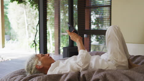 senior biracial woman lying in bed using tablet