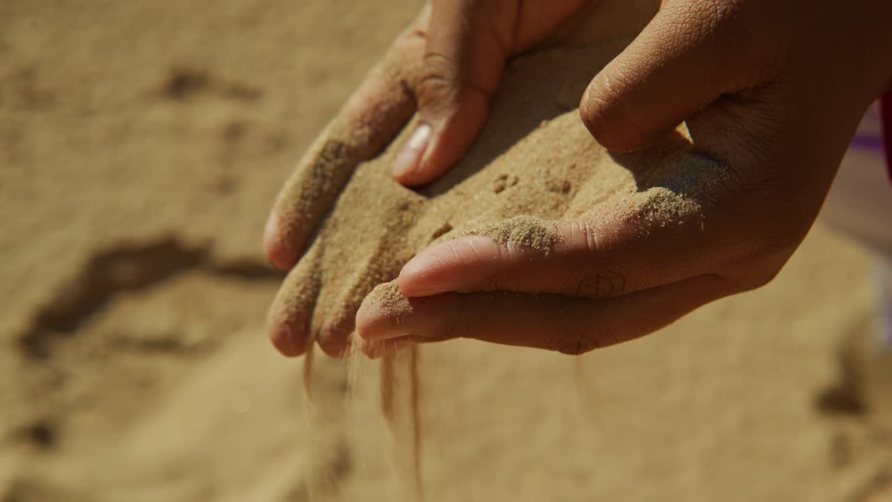 Närbild på händer som siktar gyllene sand mellan fingrarna