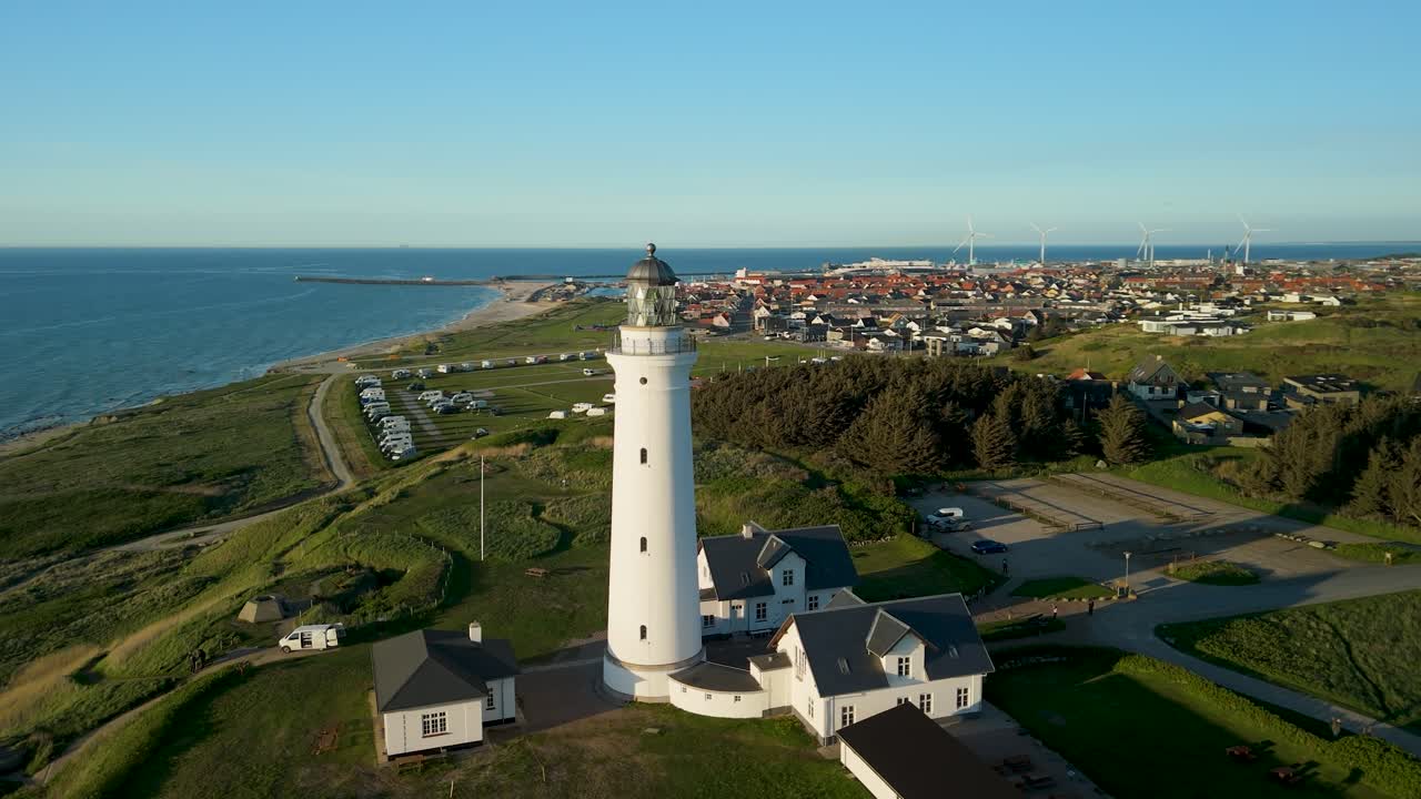 Luftbåret parallax omkring det historiske hvide Hirtshals Fyr i den gyldne time, der fanger barske kystklitter og Skagerrak-havet i Nordjylland, og viser en klassisk skandinavisk kystsolnedgang