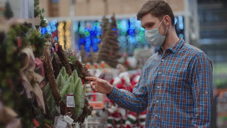 un hombre con una máscara protectora en una joyería y guirnaldas con juguetes para árboles de navidad y en casa. guirnaldas navideñas y decoración